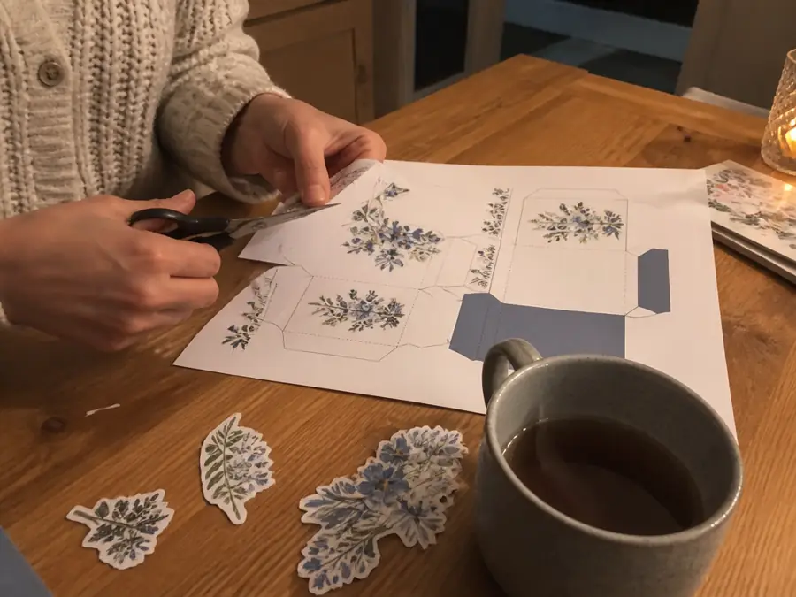Hands cutting out a printed card template at the kitchen table